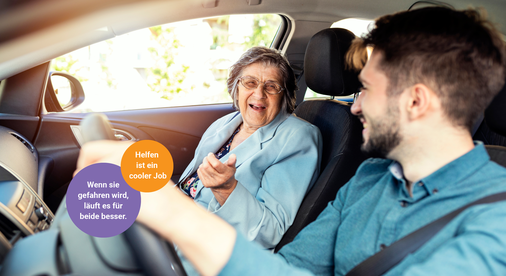 Ein junger Mann am Steuer eines Autos lacht gemeinsam mit einer älteren Dame, die auf dem Beifahrersitz sitzt.